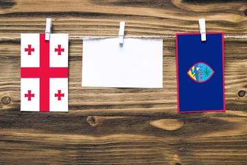 Hanging flags of Georgia and Guam attached to rope with clothes pins with copy space on white note paper on wooden background.Diplomatic relations between countries.