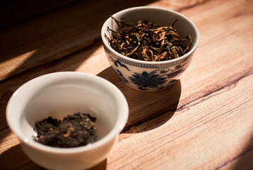 Dry tea leaves in tea cups on wooden table