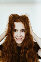 beautiful young lady with brown eyes ruffles her luxurious red hair with her hands