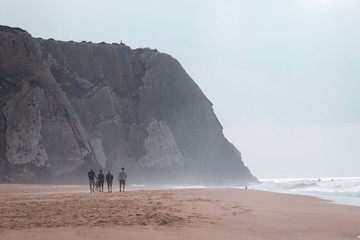 Beach with a big cliff in background in a winter day with four people walking. Paria Grande Sintra Portugal - obrazy, fototapety, plakaty