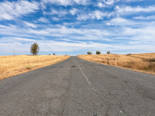 asphalt road in a dry countryside with blue sky in background