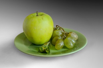 A green Apple, a grape, a withered leaf on a green plate