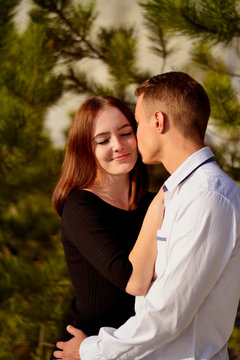 A young man kisses a beautiful laughing girl on the neck 