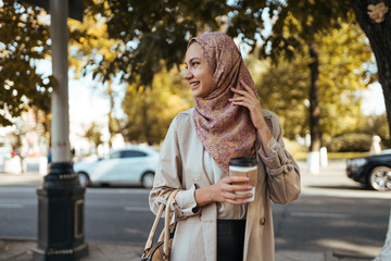 muslim woman with a happy smile is drinking coffee on the street