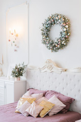 Pink and white Christmas decor in the classic bedroom, pillows on the bed and a wreath over the bed