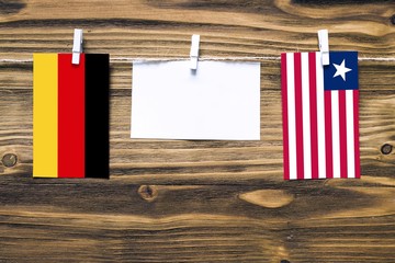 Hanging flags of Germany and Liberia attached to rope with clothes pins with copy space on white note paper on wooden background.Diplomatic relations between countries.