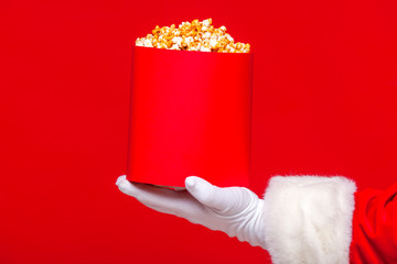Christmas. Photo of Santa Claus gloved hand With a red bucket with popcorn, on a red background