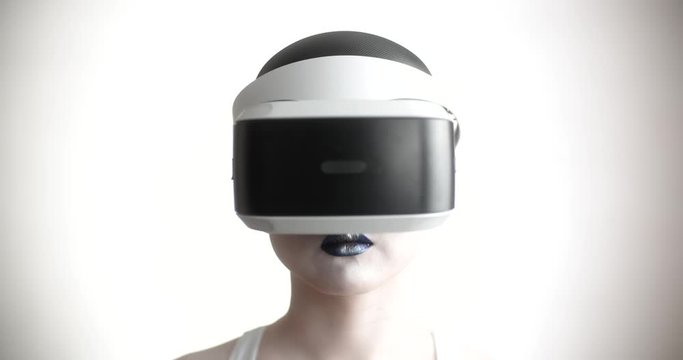 Young asian girl with bright artistic make-up wearing a vr helmet diving in world of vitual reality, moving her hands and interacting with it - technology concept closeup 4k footage