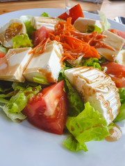 View of a healthy and light homemade meal on a wooden table. Fresh cheese salad with tomatoes from the garden, carrot, lettuce and cooked egg.