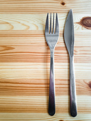 Vertical stock photography. Metal knife and fork placed on a wooden table in an overhead view.