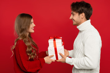 side view of happy young couple gifting Christmas presents isolated on red background. Christmas concept