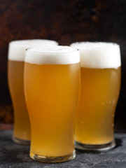 three glasses of light unfiltered beer close up on a dark background