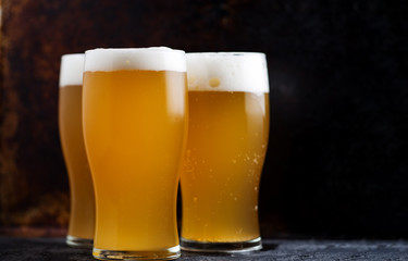 three glasses of light unfiltered beer close up on a dark background