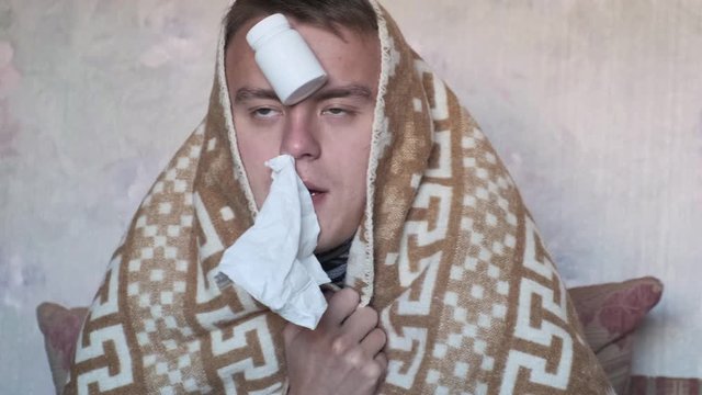 Funny young man with flu or cold symptoms in a plaid coughs, closeup