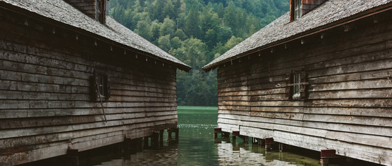 Two wooden gray houses on the water in the wooded alpine mountains of Austria. Boathouse