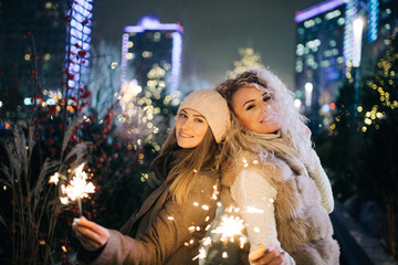 Photo of two women with Bengal lights on winter walk on background of decorated spruce