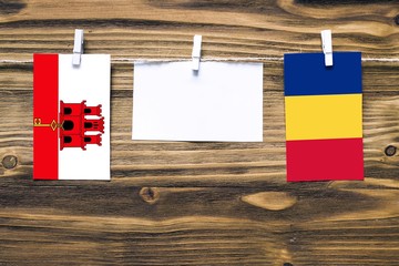 Hanging flags of Gibraltar and Romania attached to rope with clothes pins with copy space on white note paper on wooden background.Diplomatic relations between countries.