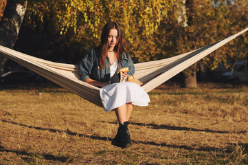 Young woman reading book in comfortable hammock in the park.