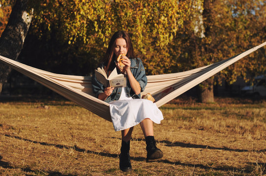 Young woman reading book in comfortable hammock in the park.