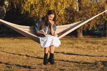 Young woman reading book in comfortable hammock in the park.