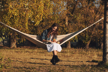 Young woman reading book in comfortable hammock in the park.