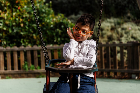ni&ntilde;o en columpio riendo haciendole cosquillas en parque. con discapacidad, con gafas.