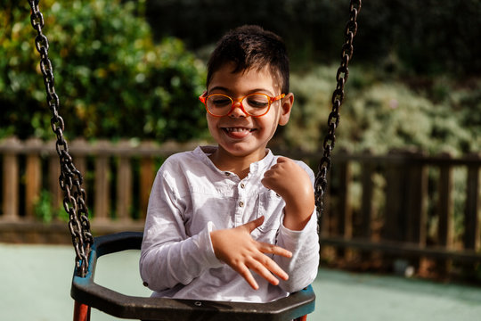 ni&ntilde;o en columpio riendo haciendole cosquillas en parque. con discapacidad, con gafas.