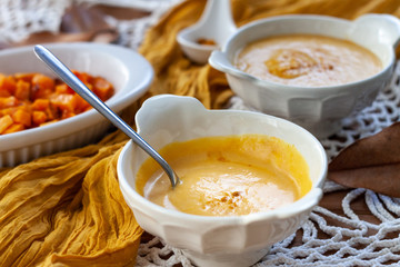 Pumpkin cream spiced with curry in a white bowl with a spoon and some roasted pumpkin dice and croutons. Close Up