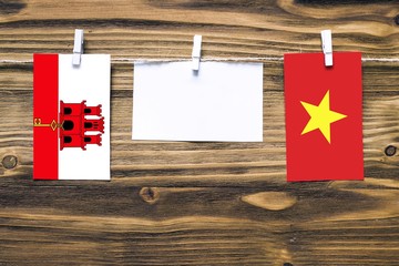 Hanging flags of Gibraltar and Vietnam attached to rope with clothes pins with copy space on white note paper on wooden background.Diplomatic relations between countries.