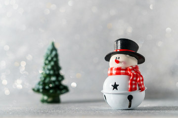 A toy snowman in a black hat stands near a candle in the form of a fir tree on a background with beautiful bokeh.