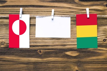 Hanging flags of Greenland and Guinea attached to rope with clothes pins with copy space on white...