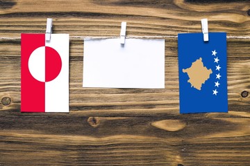Hanging flags of Greenland and Kosovo attached to rope with clothes pins with copy space on white note paper on wooden background.Diplomatic relations between countries.