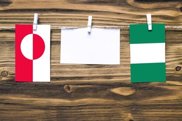 Hanging flags of Greenland and Nigeria attached to rope with clothes pins with copy space on white note paper on wooden background.Diplomatic relations between countries.