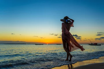 Foto op Canvas Mooi meisje in een strohoed en pareo op het strand tijdens zonsondergang van het eiland Zanzibar, Tanzania, Oost-Afrika © OlegD