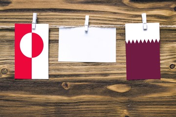 Hanging flags of Greenland and Qatar attached to rope with clothes pins with copy space on white...