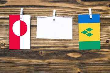 Hanging flags of Greenland and Saint Vincent And The Grenadines attached to rope with clothes pins with copy space on white note paper on wooden background.Diplomatic relations between countries.