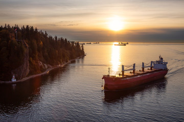 Vancouver, British Columbia, Canada. Aerial View from Above of a Cargo Ship arriving to the Port near Stanley Park during a vibrant sunny sunset.