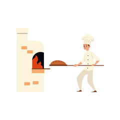 A young Caucasian male baker in bakery or kitchen carries loaf of bread on a shovel in oven.