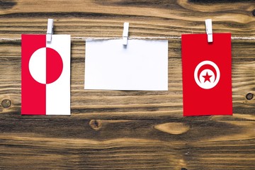 Hanging flags of Greenland and Tunisia attached to rope with clothes pins with copy space on white note paper on wooden background.Diplomatic relations between countries.