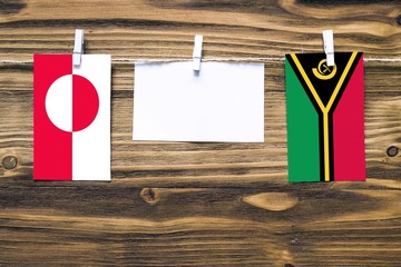 Hanging flags of Greenland and Vanuatu attached to rope with clothes pins with copy space on white...