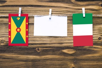 Hanging flags of Grenada and Italy attached to rope with clothes pins with copy space on white note paper on wooden background.Diplomatic relations between countries.