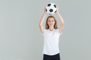 Young woman in a white shirt lifted a soccer ball up above her head.