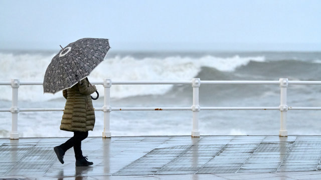 Mujer con paraguas caminando por la acera durante un temporal de olas