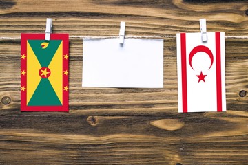 Hanging flags of Grenada and Northern Cyprus attached to rope with clothes pins with copy space on white note paper on wooden background.Diplomatic relations between countries.