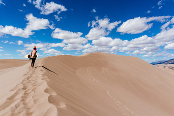 Woman walking up a dune with a sand board