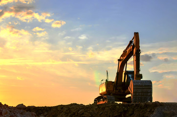 Heavy excavator working at construction site on a background  sunset. Crushing and processing of...