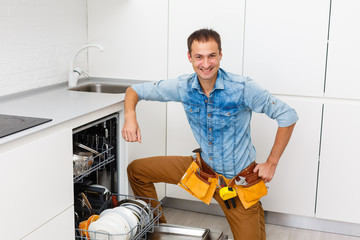 smiling handsome plumber standing with crossed arms and looking at camera in kitchen
