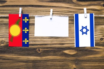 Hanging flags of Guadeloupe and Israel attached to rope with clothes pins with copy space on white...