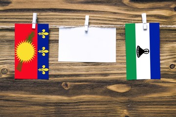 Hanging flags of Guadeloupe and Lesotho attached to rope with clothes pins with copy space on white...