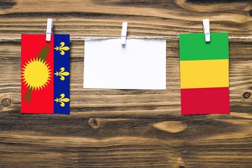 Hanging flags of Guadeloupe and Mali attached to rope with clothes pins with copy space on white note paper on wooden background.Diplomatic relations between countries.